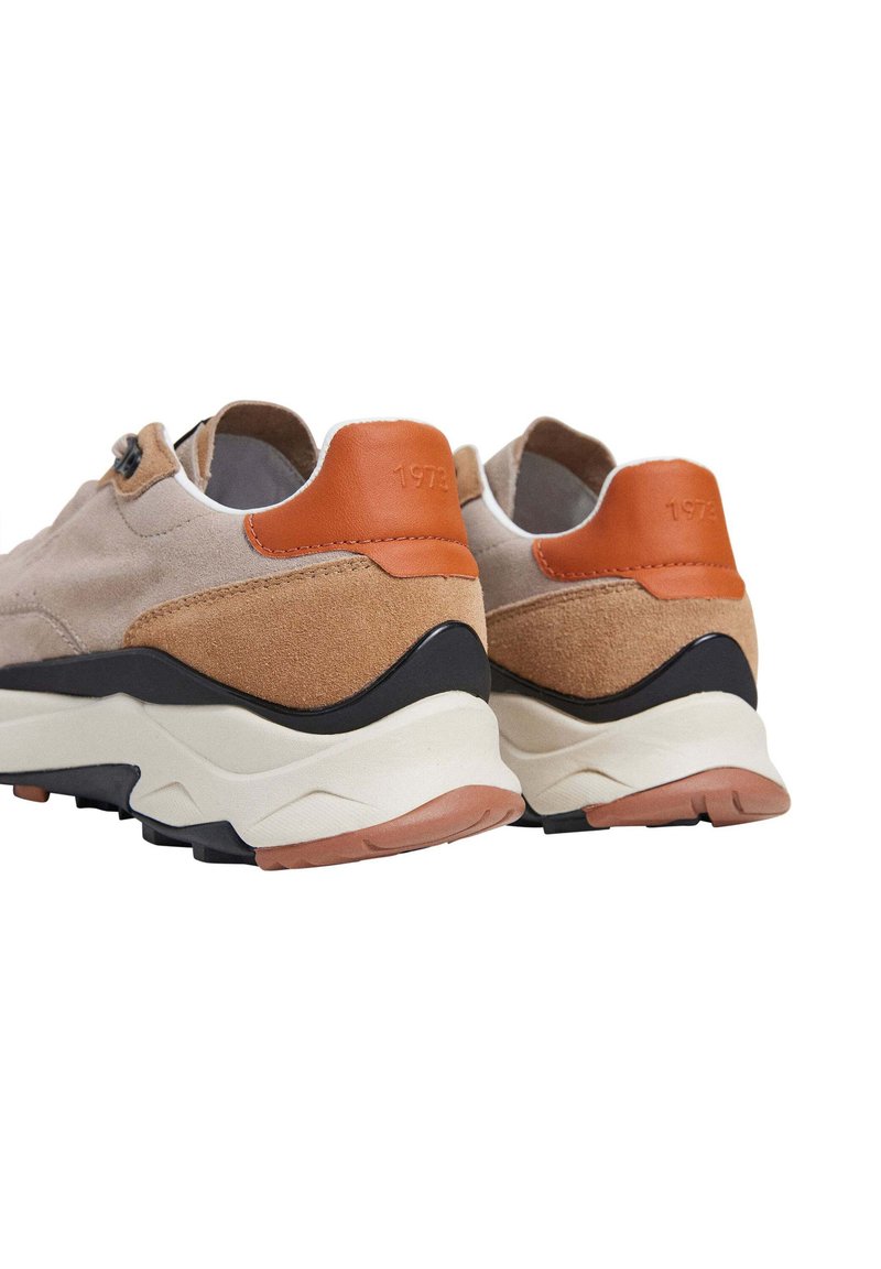 Zapatos de ante beige claro con un acento en el tacón de cuero marrón y suela de goma negra. Presentan un diseño texturizado y un detalle en relieve en el tacón.