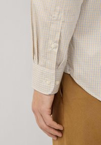 Camisa de manga larga con un patrón de cuadros amarillos y azules, puños con botones y una textura de tela suave. Combinada con pantalones caqui.