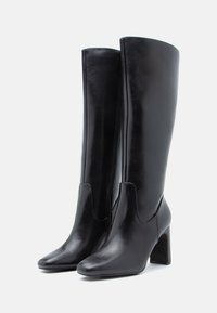 Μαύρες δερμάτινες μποτές μέχρι το γόνατο με κομψό σχέδιο, στρογγυλή μύτη και χοντρό ψηλό τακούνι. Διαθέτουν φερμουάρ στο πλάι και λεία υφή.