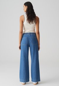 Pantalons en denim à jambes larges de couleur bleu clair avec une taille élastique haute, dotés de deux poches arrière et d'une texture denim classique.