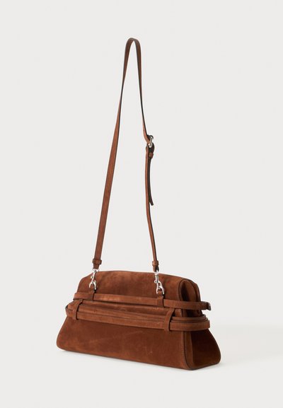 Sac à épaule en daim marron avec une longue bandoulière réglable et un détail de sangle horizontale, présenté sur un fond clair uni.