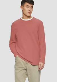 Langärmliges Crewneck-Shirt in Rostfarbe, aus strukturiertem Stoff. Verfügt über einen kontrastierenden weißen Innenkragen und einen lockeren Schnitt.