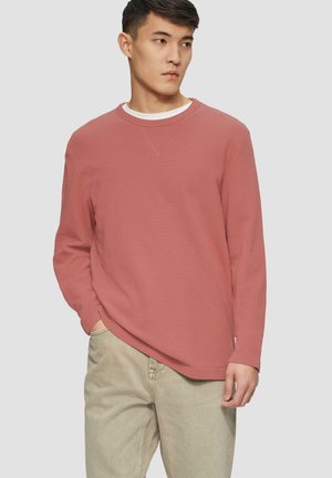 Oversized langslavige t-shirt in roestkleur, gemaakt van textuurstof. Heeft een contrasterende witte binnenkraag en een relaxte pasvorm.