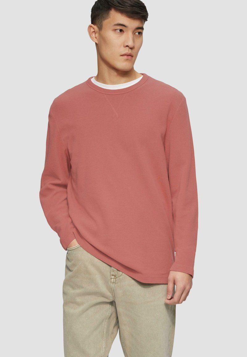 Langärmliges Crewneck-Shirt in Rostfarbe, aus strukturiertem Stoff. Verfügt über einen kontrastierenden weißen Innenkragen und einen lockeren Schnitt.