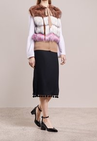 Faux fur-lagerad topp i brunt, vitt och rosa med en ribbad brun bas. Svart plisserad kjol med pom-pom-kant. Svarta lakläderklackar.