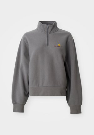 Sivi Carhartt dukserica s četvrtastim patentnim zatvaračem, dugih rukava, rebrastim završecima rukava i donjeg dijela, te s malim žutim i crvenim logotipom na prsima.