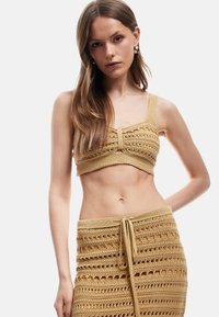 Set in maglia all'uncinetto a due pezzi in un tenue color sabbia, composto da un top corto con spalline larghe e una gonna aderente con lacci e dettagli in lavorazione aperta.