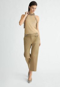 Top halter beige con scollatura a volant, abbinato a pantaloni a gamba larga marrone chiaro e tacchi con stampa pitone, ambientato su uno sfondo neutro.