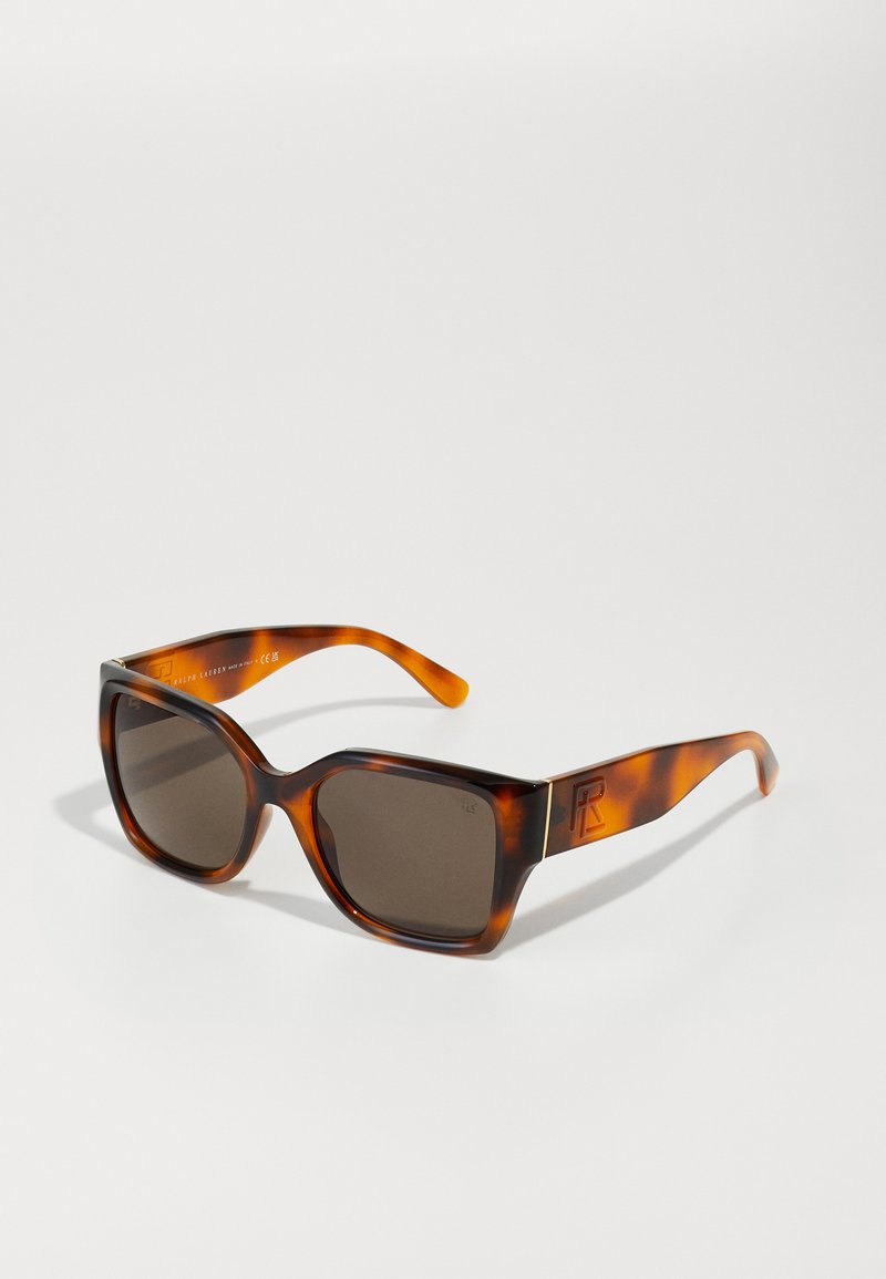 Kilpkonnakilbi moega prillid, paksu ruudukujulise raamiga, tumedate läätsedega ja logo aktsendiga templil. Sile tekstuur, millel on kerge läbipaistvus.