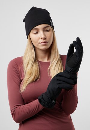 Guanti neri con un polsino foderato in morbido pelo e una superficie liscia e resistente all'acqua. Indossati da una persona con un top a maniche lunghe color bordeaux.