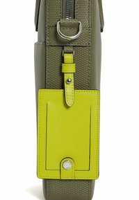 Bolso texturizado verde con cierre de cremallera, anilla en D lateral y una etiqueta de cuero amarilla brillante con detalle de botón a presión.