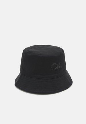 Sort bøllehat med påsyet "CK" logo på siden, med en blød, bred skygge og glat stoftekstur.