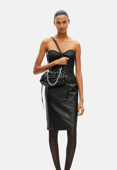 Robe en cuir noir à silhouette ajustée, associée à un sac à main noir texturé avec une chaîne métallique et une fermeture à cordon.