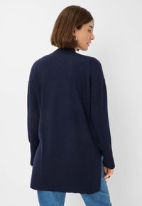 Cardigan lavorato a maglia blu navy con orlo a costine, maniche lunghe e vestibilità rilassata. Il retro presenta un collo alto e un design di lunghezza media.