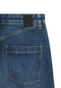 Mörkblå jeans i denim med en texturerad yta. Har en svart läderlogopatch märkt "BOSS" vid bakre midjan och en enda bakficka.