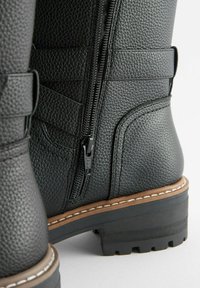 Schwarze Lederstiefeletten mit strukturierter Oberfläche, ausgestattet mit einem seitlichen Reißverschluss und einer kontrastierenden hellbraunen Sohle mit sichtbaren Profilmustern.
