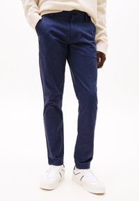 Tmavomodré bavlnené chino nohavice s úzkym strihom, vybavené bočnými vreckami a zapínaním na gombík. Kombinované s bielymi teniskami pre kontrast.