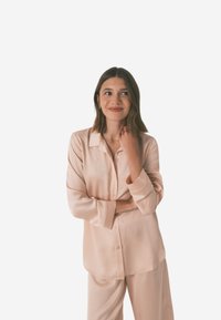 Lyserød satin skjorte med knap-ned design, lange ærmer og løs pasform, parret med matchende lyserøde bukser.