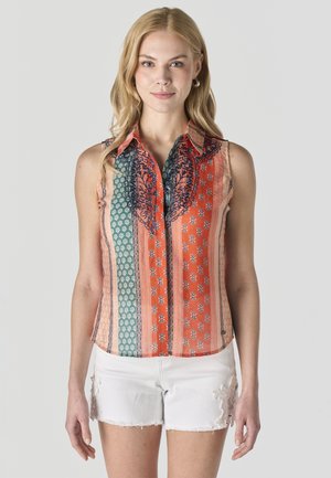 Joven mujer que lleva una blusa sin mangas con cuello, de estampado multicolor, y pantalones cortos de mezclilla blancos con bordado floral en el lateral.