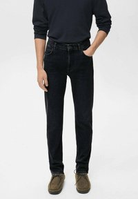 Jeans de mezclilla negra con corte recto, cinco bolsillos y una cintura de altura media, combinados con zapatos mocasines de gamuza marrón.