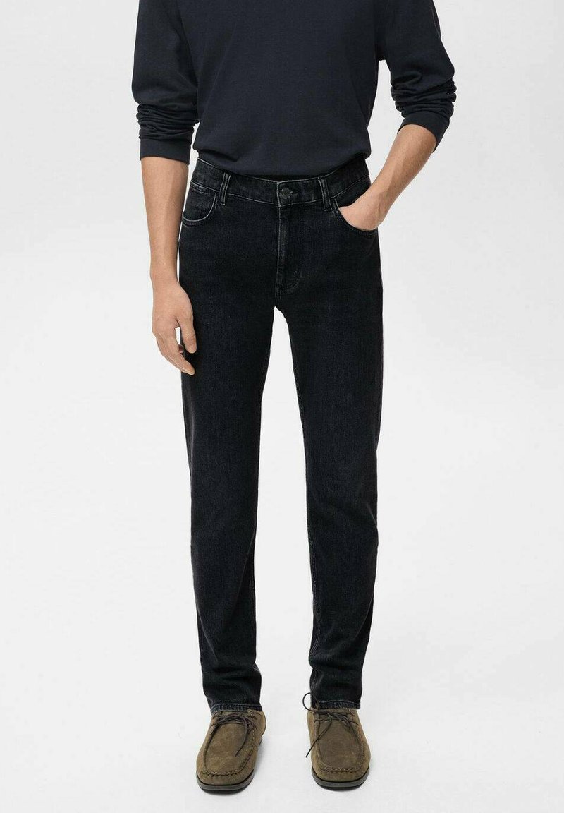Jeans de mezclilla negra con corte recto, cinco bolsillos y una cintura de altura media, combinados con zapatos mocasines de gamuza marrón.