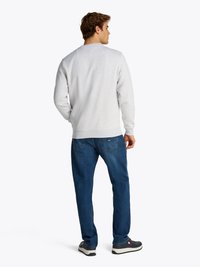 Felpa grigia con collo rotondo, polsini e orlo a coste. Abbinata a jeans blu e sneakers grigie. Design minimalista senza motivi.