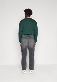 Camicia verde a maniche lunghe, jeans grigi dalla vestibilità rilassata, sneakers bianche con accenti verdi. Focus sullo stile casual e sul contrasto dei colori.