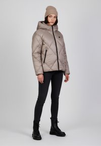 Giacca puffer beige chiaro con cappuccio, caratterizzata da trapuntature diagonali, tasche con zip nere, abbinata a jeans skinny neri e stivali neri stringati.