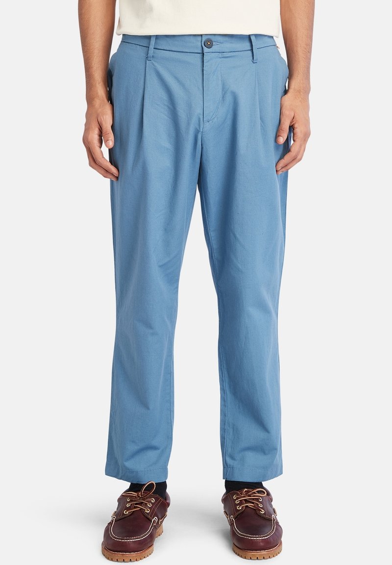 Jasnoniebieskie plisowane spodnie wykonane z miękkiej tkaniny, z zamkiem błyskawicznym i guzikiem, o prostym kroju nogawki i kieszeniach.