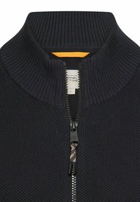 Marineblauwe trui met ritssluiting, een geribbelde kraag en een gestructureerde stof. Heeft een gele accent onder de kraag en een stevige zwarte ritssluiting.