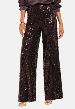 Woman wearing high-waist, wide-leg black sequin pants with a dark long-sleeve top and gold open-toe heels.