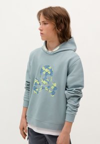 Jasnoniebieska bluza z kapturem wykonana z miękkiego materiału, z kolorowym wzorem czaszki i skrzyżowanych kości w odcieniach niebieskiego i żółtego. Dodatkowo ma ściągacze przy mankietach i dolnej krawędzi.