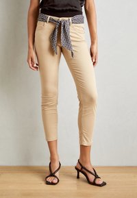 Beige kapealaiset housut musta-valkoisella kuvioidulla vyösoljella, jossa on sileä pinta ja kapeat nilkkapituudet. Yhdistetty korkokenkiin.