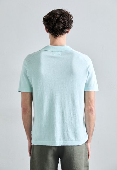 Tricou scurt cu mânecă, de culoare bleu deschis, realizat dintr-un material texturat. Dispune de un guler clasic și cusături plate la umeri și spate.