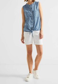 Hihaton farkkipaita, vaaleansininen, jossa on kaksi rintataskua ja solmittu etuosa. Yhdistetty valkoisiin käärittäviin shortsit ja valkoisiin lenkkareihin.