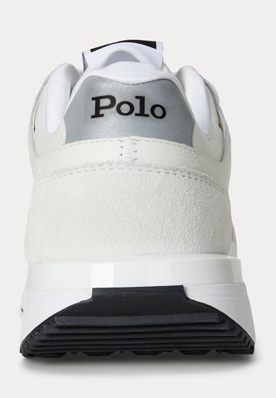 Baskets blanches avec une semelle noire, languette de talon grise et logo "Polo" en texte noir sur la partie arrière du talon.