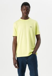 Limegrønn bomull t-skjorte med korte ermer og rund hals, med en liten svart "BOSS" logo på venstre bryst. Kombinert med mørke jeans.