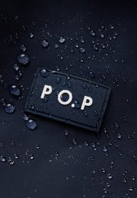 Marine waterafstotende stof met gegraveerde diagonale strepen, voorzien van een rechthoekig zwart label en witte letters "P.O.P." met waterdruppels.