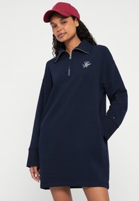 Robe sweat-shirt marine avec col zippé, ornée d'un logo sur la poitrine et de manches longues. Tissu lisse avec une coupe décontractée.