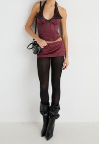 Haut halter à pois bordeaux associé à une mini jupe assortie, des collants noirs opaques et des bottes noires décontractées. Petit sac à main rond.