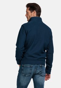 Navyblauwe pullover met hoge kraag, geribde manchetten en gestructureerde stof, gecombineerd met lichtblauwe spijkerbroek.