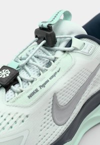 Svijetlo mentol zelena atletska cipela s teksturiranim mrežastim gornjim dijelom, siva akcentna boja i siguran sustav vezivanja. Na strani se nalazi Nike logo.