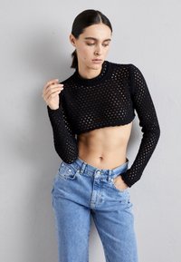 Svart strikket kort jakke med lange ermer, med åpen vevstruktur. Kombinert med høytlivs lys blå denimjeans.