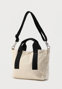 Τσάντα ώμου από καμβά σε μπεζ χρώμα με μαύρες λαβές και ρυθμιζόμενο ιμάντα ώμου. Διαθέτει ανθεκτικές ραφές και συμπαγή ορθογώνιο σχήμα.