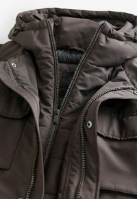 Braune isolierte Jacke mit Reißverschluss, Kapuze mit Kordelzügen, strukturiertem Stoff, Fronttaschen und glatter Innenauskleidung.