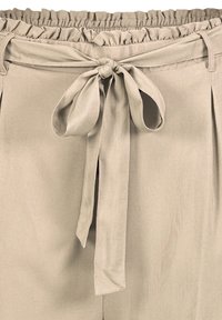 Beige pants with a ruffled elastic waistband and a fabric bow tie detail at the front, made from smooth, lightweight material.