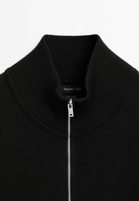 Black knit zip-up sweater with a high collar. Features a silver zipper, ribbed texture, and a label reading "Massimo Dutti, 100% Cotton."