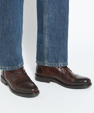 Bottes montantes en cuir marron portées avec un jean denim bleu, posées sur une surface claire.