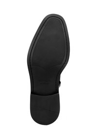 Suela de zapato negra con goma texturizada para agarre, acabado de cuero liso y ribete cosido. Presenta el nombre de la marca en relieve "WITTCHEN handmade".