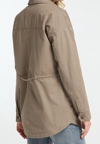 Khaki-farbene Freizeitjacke mit geradem Schnitt, großem Kragen und zwei Seitentaschen. Hergestellt aus leichtem Stoff; mit Knopfmanschetten und einem Rückenteil.